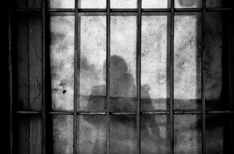 A shadow of a person seen against a wall with metal bars in front