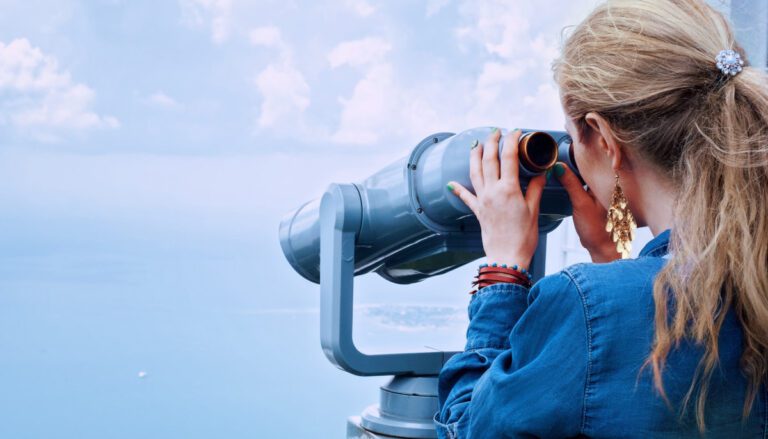 Person in denim jacket looking through public viewing binoculars.