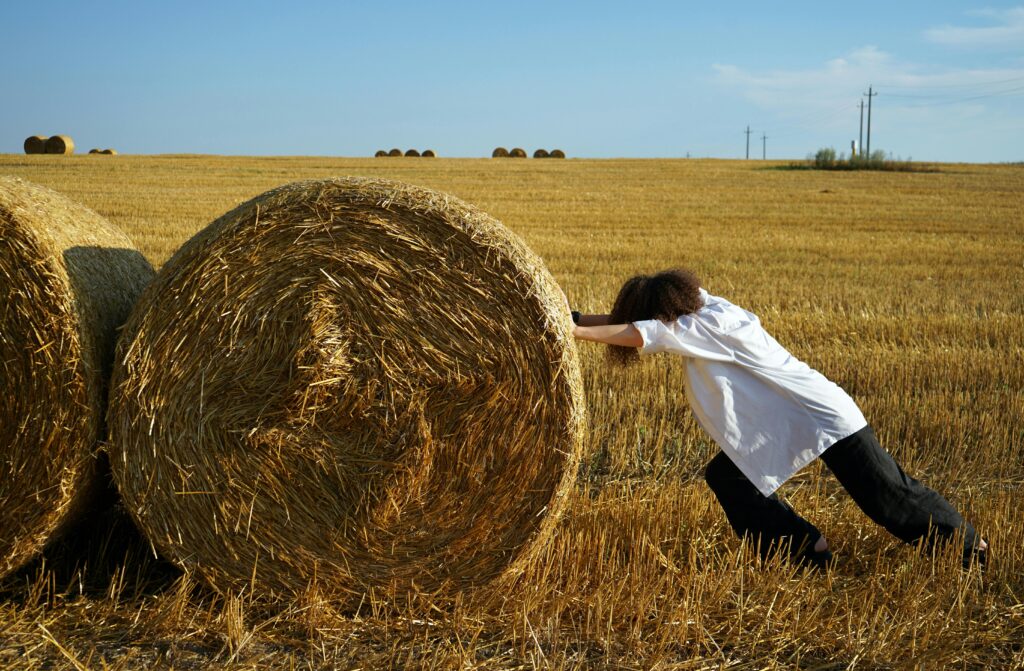 Person pushing hard, with both hands, to try to move giant bales of hay.